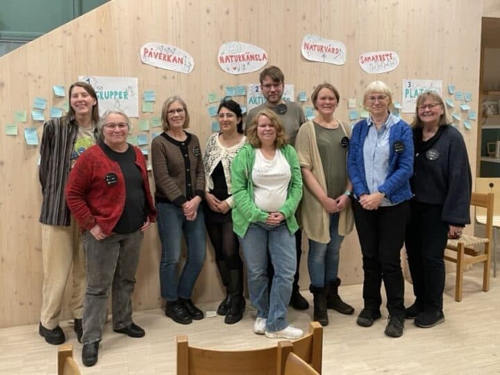 Bilden visar en grupp på åtta personer som står tillsammans och poserar för ett fotografi. De ...