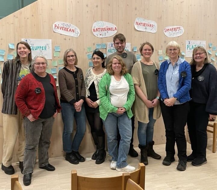 Bilden visar en grupp på åtta personer som står tillsammans och poserar för ett fotografi. De ...